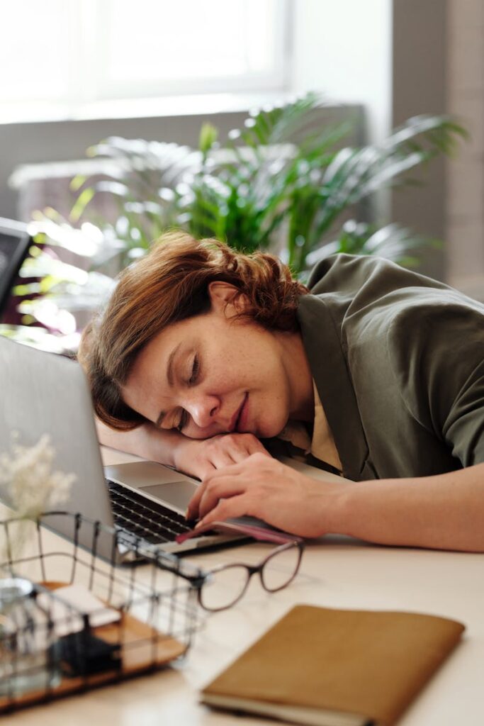Tired woman in home office resting on laptop, illustrating burnout.