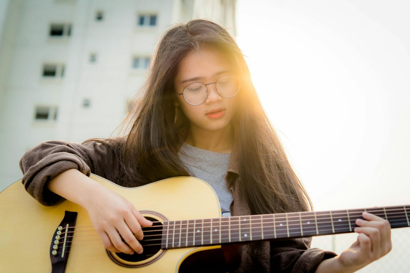 Portrait of a young woman with glasses playing guitar outdoors at sunset.