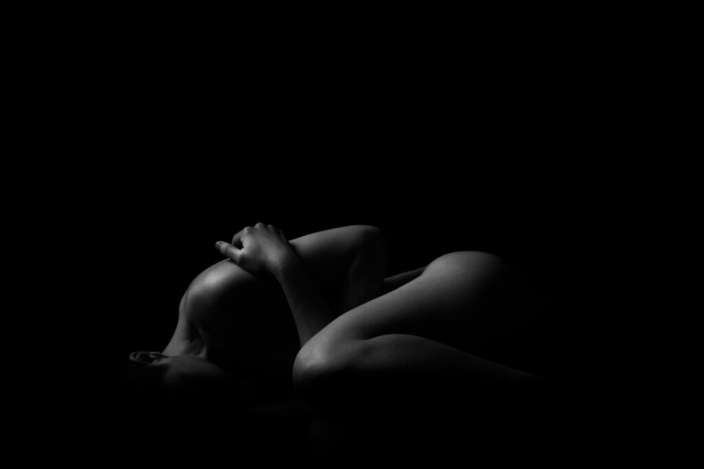 Artistic black and white nude photograph featuring a silhouette of a woman in a studio.